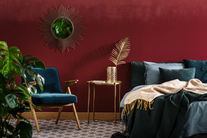 Chambre avec murs rouges, literie aux tons de bijoux et chaise d'appoint.