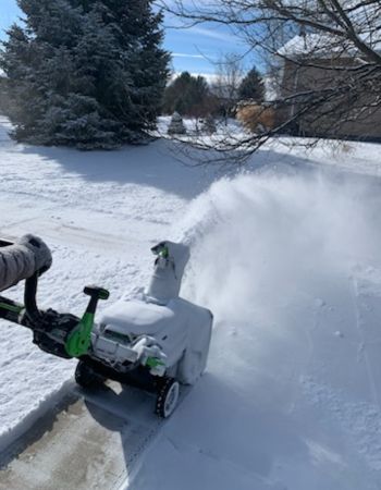 Quelqu'un utilise la souffleuse à neige légère Ego pour souffler la neige d'un trottoir.