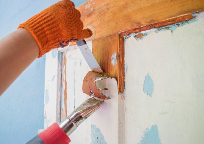 Le processus de nettoyage d'une vieille porte en bois des couches de peinture. Enlèvement du revêtement avec un sèche-cheveux et une spatule. Les mains de l'ouvrier dans des gants orange avec un outil. Rénovation de la maison.