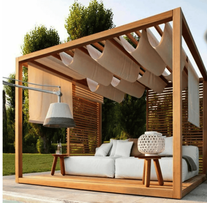 Superbe pergola avec un canapé blanc moelleux en dessous et un tissu blanc suspendu aux lattes au-dessus.