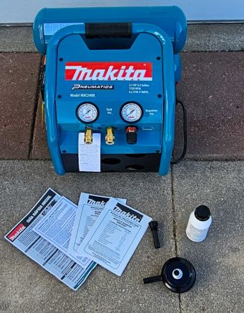 Le compresseur d'air Makita MAC2400 2,5 CV avec son manuel d'instructions et les extras inclus sur une surface en ciment avant le test.