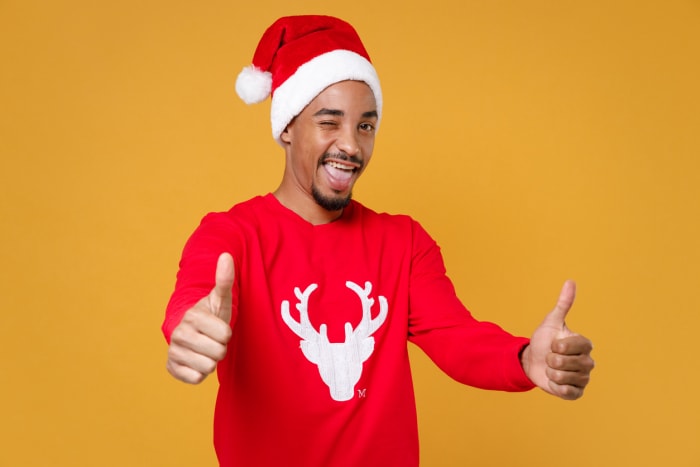 Portrait en studio d'un jeune Père Noël afro-américain de 20 ans en pull rouge avec un chapeau de cerf montrant les pouces levés isolé sur fond jaune. Concept de joyeuses fêtes de fin d'année.