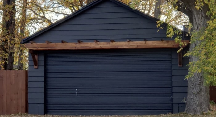 Pergola en bois marron au-dessus de la porte d'un garage moderne gris anthracite, indépendant.