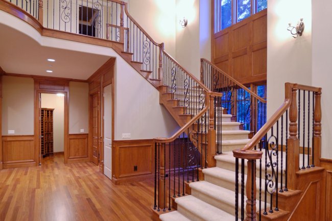 Une élégante rampe borde un escalier recouvert de moquette blanche dans une maison vide aux murs blancs et au parquet. 