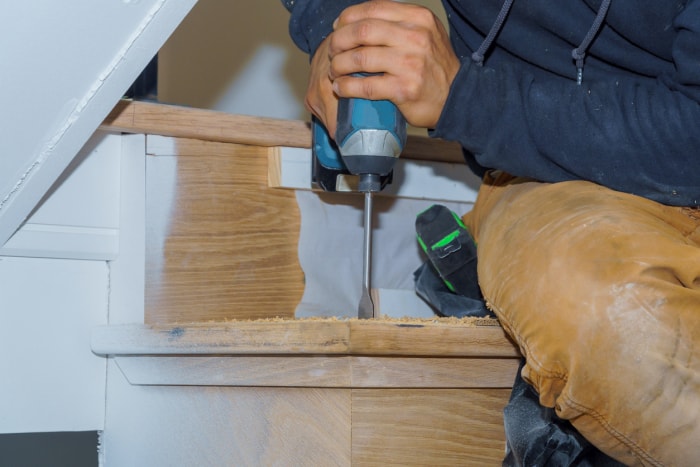 Un homme visse une marche dans une contremarche à l'aide d'une perceuse dans un escalier en bois