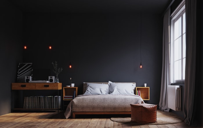 Chambre minimaliste avec draps blancs sur le lit et plafonds et murs gris foncé assortis.