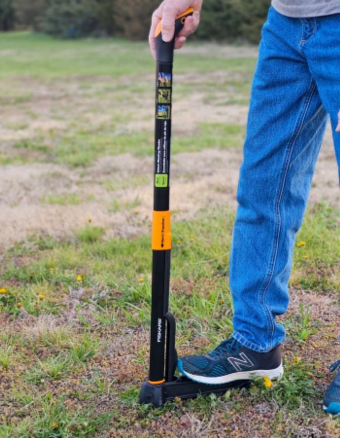 Une personne pousse l'arrache-herbe vertical Fiskars dans le sol pendant les tests.