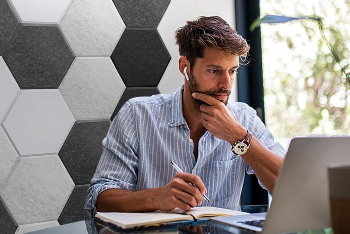 Une personne travaillant sur un ordinateur à son bureau avec des écouteurs et un mur de panneaux insonorisants hexagonaux noirs et blancs sur le mur en arrière-plan.