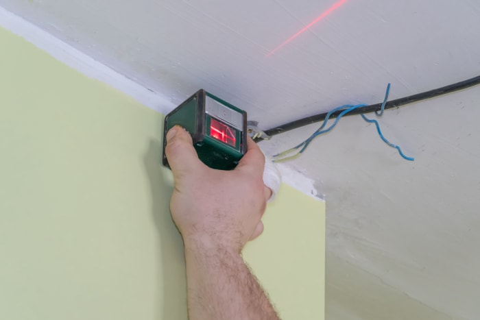 Marquage du mur avec un niveau laser pour la pose d'un plafond tendu. Lumière rouge sur le mur.