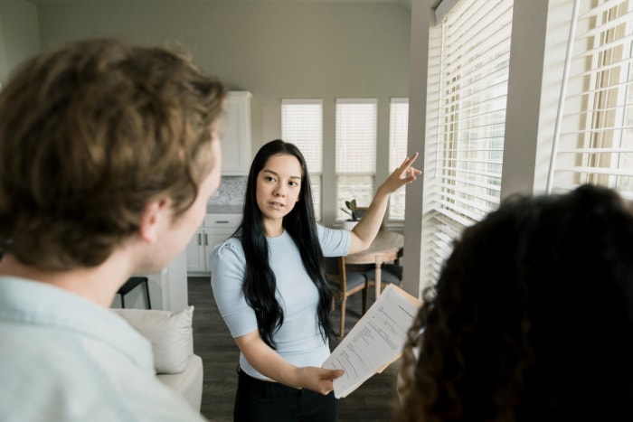 Jeune femme tenant une liste de contrôle et expliquant les caractéristiques d'une maison à un couple flou