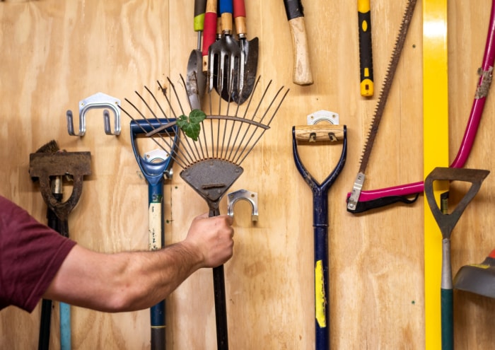 Bras masculin rangeant un râteau de jardin.