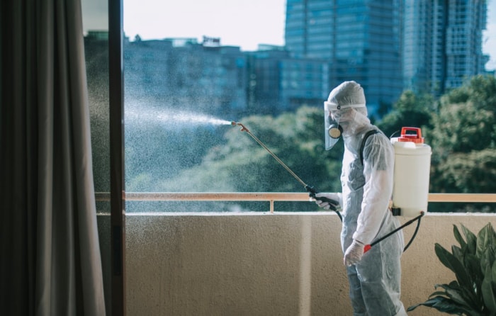 Vue d'une personne portant une combinaison de protection contre les matières dangereuses pulvérisant une solution antiparasitaire depuis un balcon. 