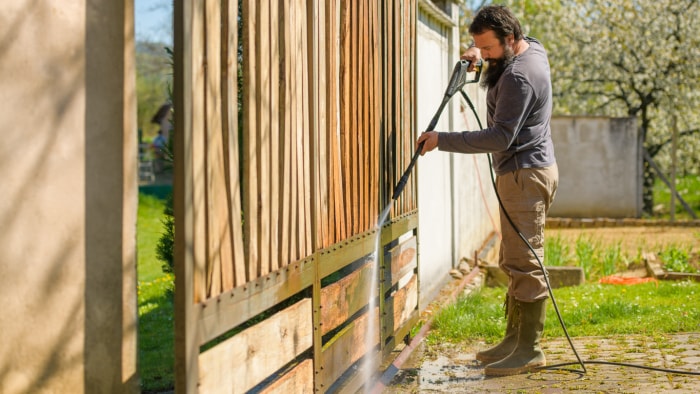 Homme d'âge moyen nettoyant une porte en bois avec un nettoyeur haute pression. Nettoyeur à eau haute pression utilisé pour réparer soi-même une porte de jardin.