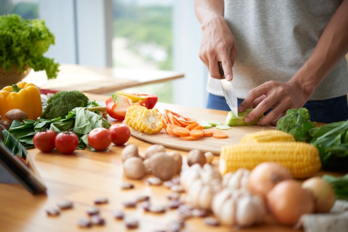 Un homme coupe des légumes sur un comptoir de cuisine.