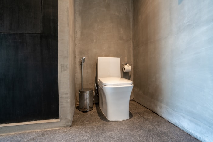 Des toilettes et une poubelle se trouvent dans un coin d'un sous-sol en béton.