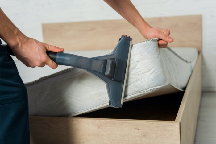 Personne passant l'aspirateur sur un matelas avec un accessoire d'aspirateur.