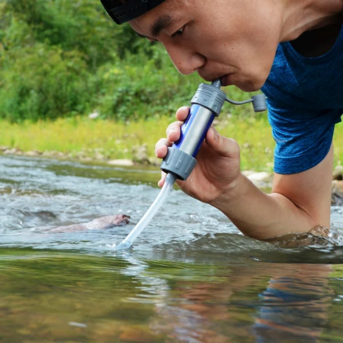 Un homme utilise un filtre à eau pour boire l'eau d'un ruisseau