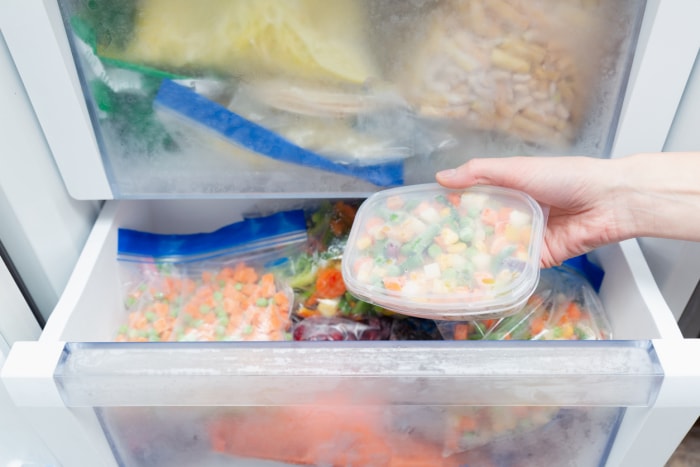 Légumes surgelés dans un sac en plastique placé à l'intérieur d'un congélateur rempli d'emballages d'aliments surgelés.