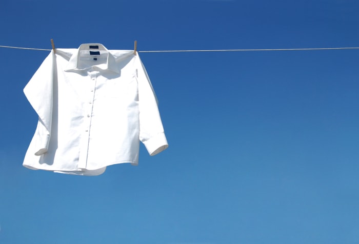 un chemisier blanc impeccable suspendu à un fil à linge devant un ciel d'un bleu éclatant