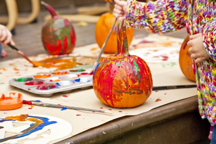 De jeunes enfants peignent de petites citrouilles de différentes couleurs sur une terrasse extérieure.