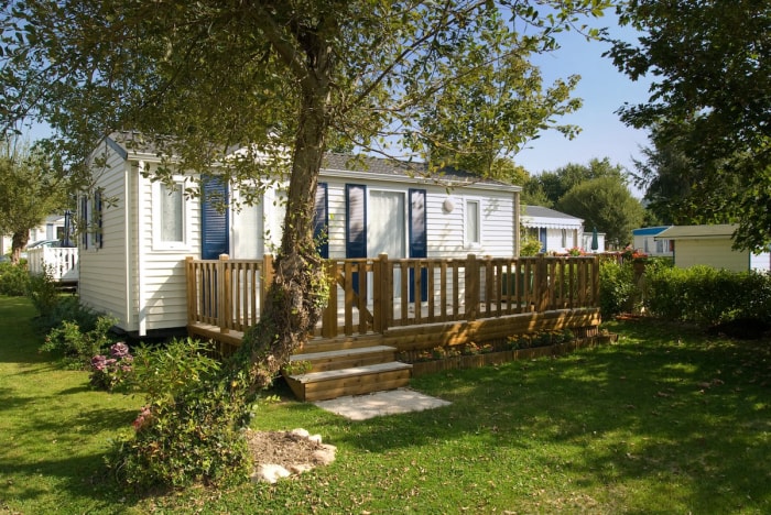 Un mobil-home blanc avec terrasse intégrée et volets bleus.