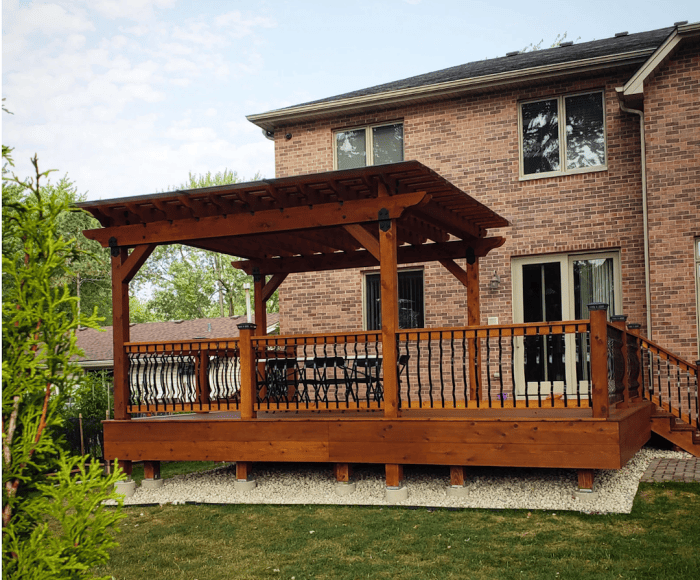 Combinaison terrasse-pergola en bois adossée à une maison en brique.