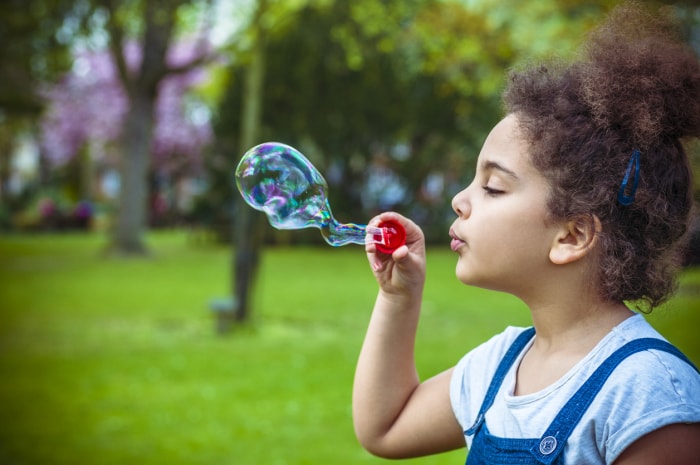 Enfant (7-8) faisant des bulles dans la cour de récréation.