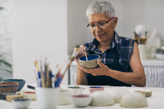 Femme âgée décorant un bol en argile dans un atelier de céramique.