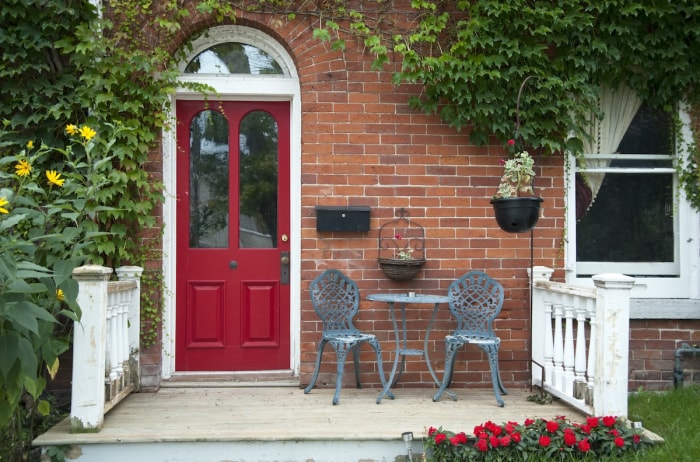 Une maison en briques avec une porte d'entrée rouge et un petit porche décoré d'une table, de chaises et de plantes.