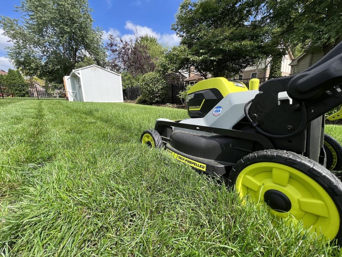 La tondeuse autopropulsée à traction intégrale Ryobi de 21 pouces en action coupant une pelouse avec de l'herbe longue et dense