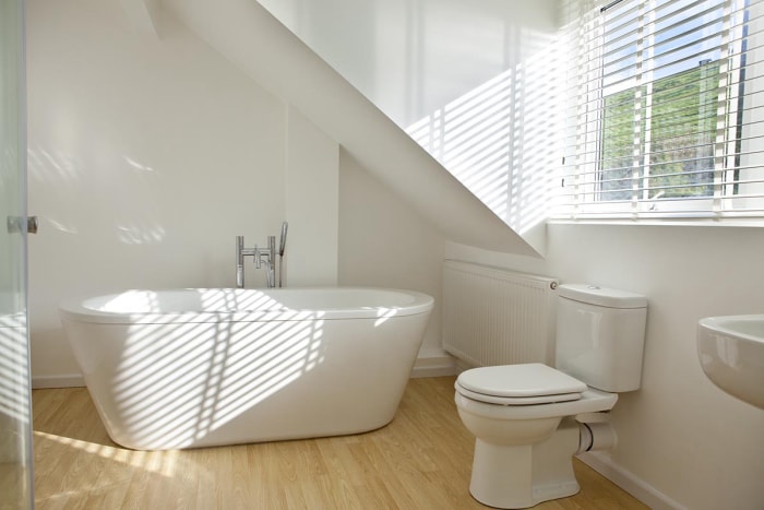 Un parquet en bois clair est installé dans une salle de bain aux murs et aux luminaires blancs. 