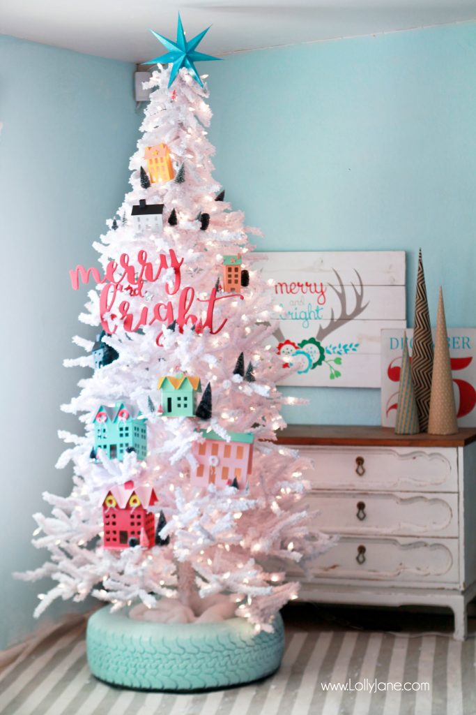 Un sapin de Noël blanc et pastel avec une base en pneu peinte en vert.