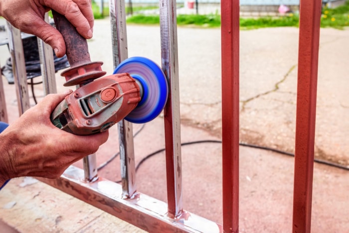 Personne utilisant une meuleuse d'angle pour enlever la peinture rouge d'une clôture métallique.