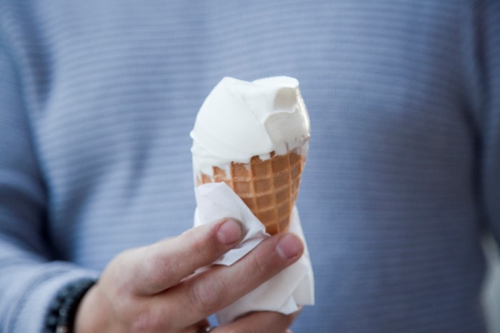 Personne en chemise bleue tenant un cornet de glace à la vanille emballé dans du papier.