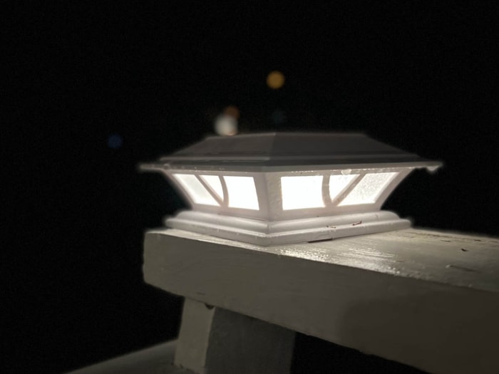 Lampe de pont blanche sur une terrasse en bois peinte en blanc illuminée la nuit