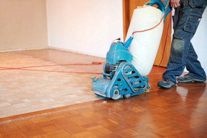 Ouvrier polissant un parquet avec une ponceuse.