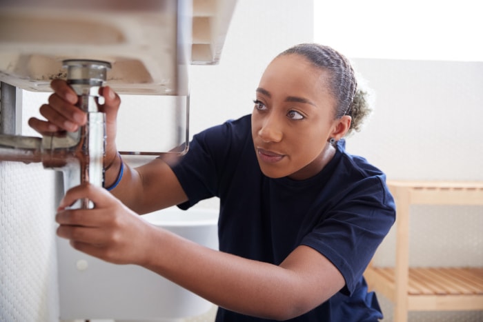 Une jeune femme inspecte la plomberie sous un évier.