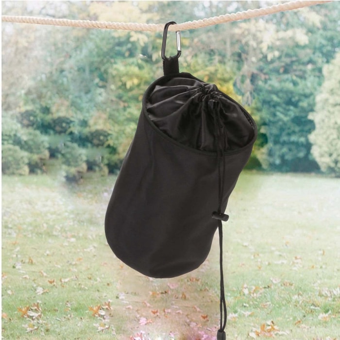 photo d'un sac à pince à linge veamor un sac cylindrique noir suspendu à une corde à linge à l'extérieur avec de l'herbe verte visible à l'arrière-plan