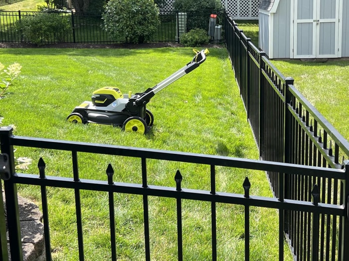 La tondeuse autopropulsée à traction intégrale Ryobi de 21 pouces dans le coin d'une pelouse soigneusement tondue à côté d'une clôture