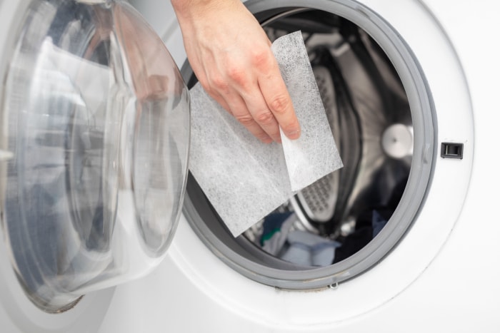 main d'une femme plaçant une feuille de sécheuse dans la sécheuse