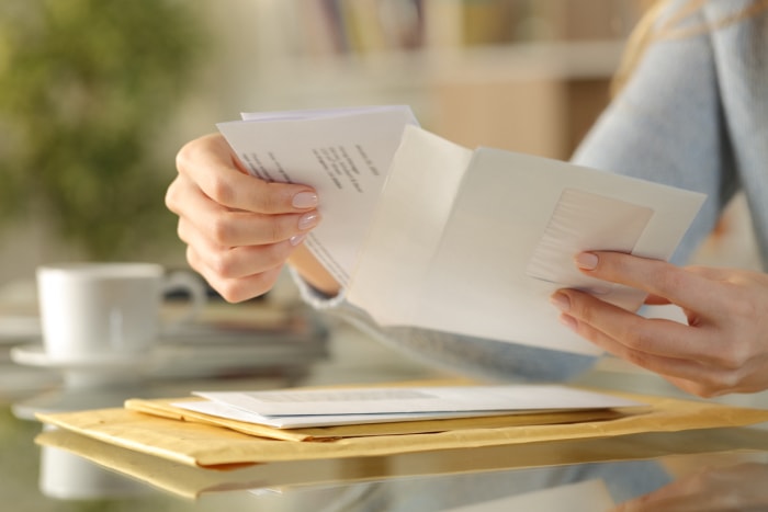 Gros plan des mains d'une femme ouvrant des factures dans le courrier alors qu'elle est assise à son bureau.