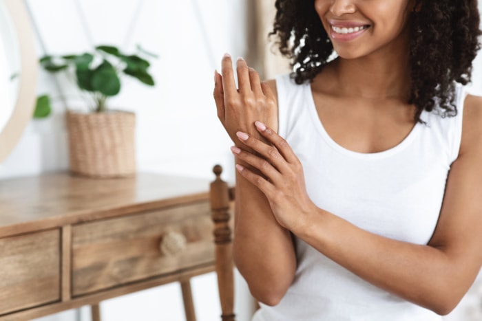 femme souriante appliquant une lotion pour les mains sur les bras et les mains