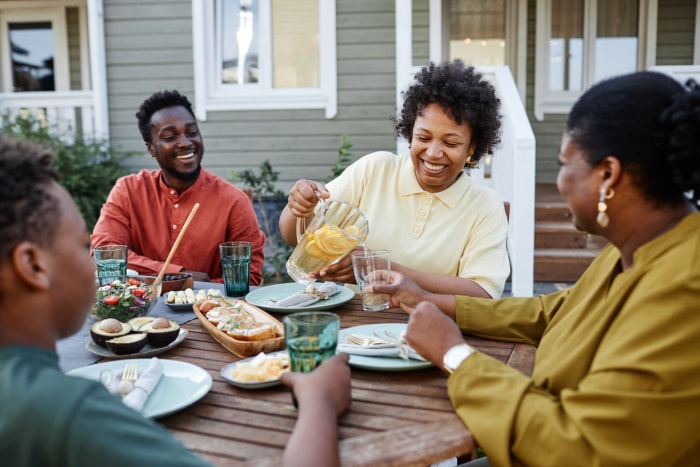 Portrait d'une femme noire souriante versant de la limonade dans un verre lors d'une réunion de famille en plein air