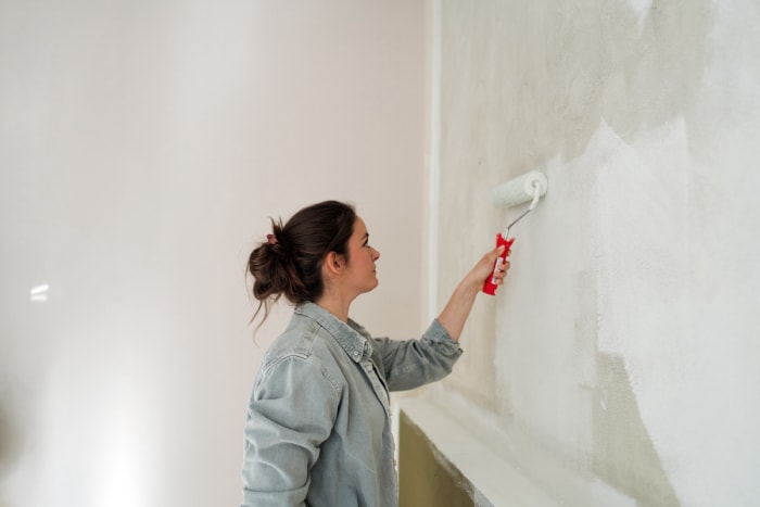 Une femme utilise un apprêt sur un mur blanc cassé avec une brosse à rouleau éponge.