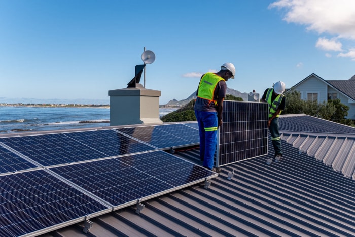 Deux ouvriers installent des panneaux solaires sur un toit. 