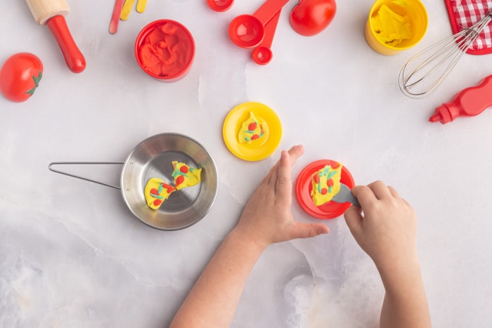 Vue aérienne des mains d'un garçon alors qu'il prépare de la nourriture factice avec de la pâte à modeler et des jouets à pâtisserie.