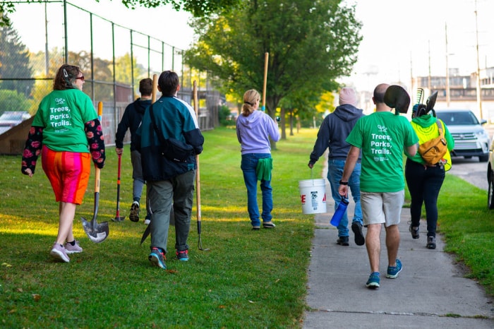 Un groupe de personnes marchant avec des pelles et des seaux sur un trottoir pour une activité Arbor Day à Grand Rapids.