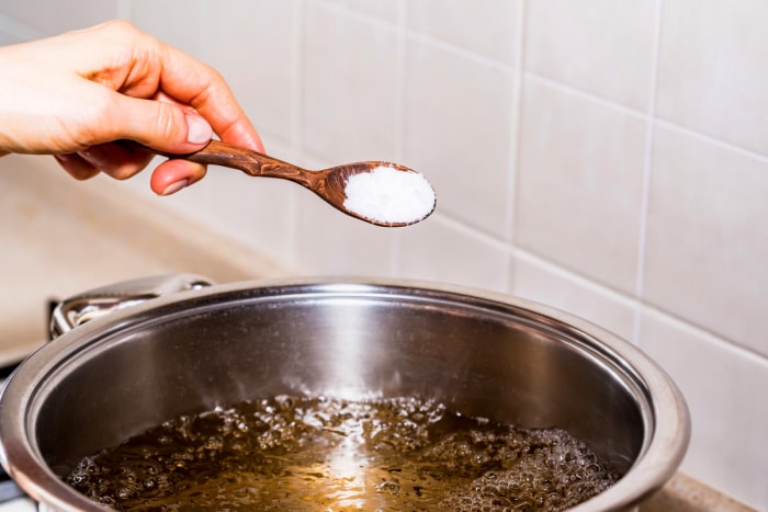 Une main ajoutant du bicarbonate de soude à de l'eau bouillante.