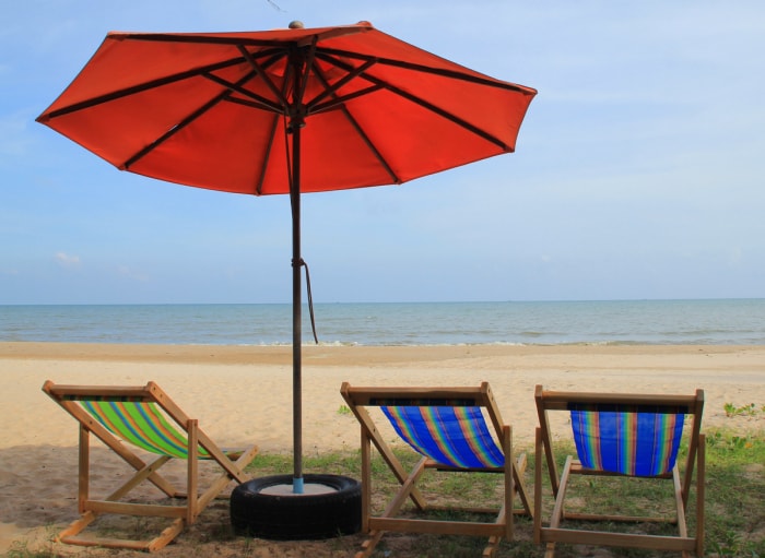 Une plage avec des chaises de patio sur le sable et un parasol dans un support en pneu recyclé.