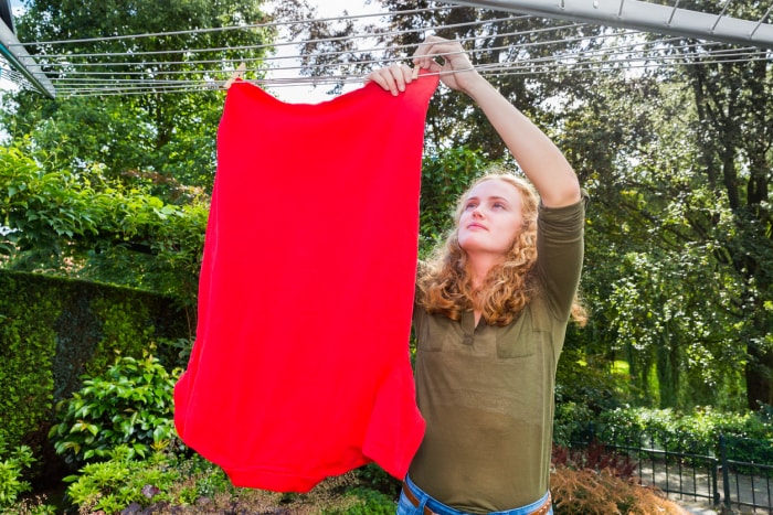 jeune femme accrochant une grande chemise rouge sur une corde à linge à l'extérieur